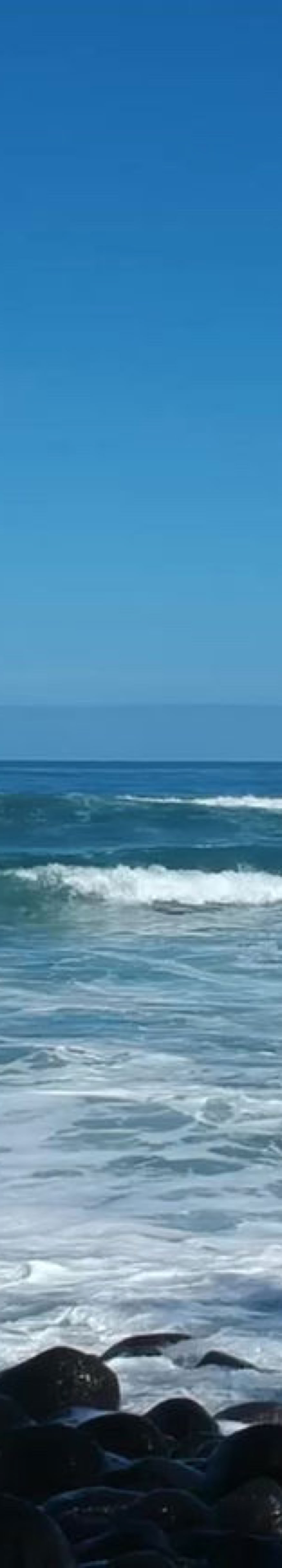 Ocean waves crashing against rocks under a clear blue sky.